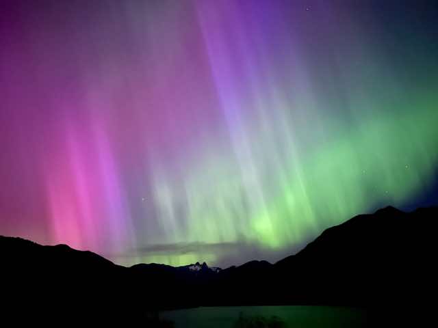 Green and pink northern lights over a dark mountain ridge